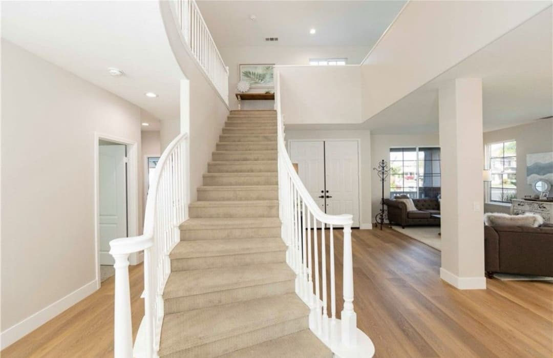 Spacious entryway featuring a carpeted staircase and open living area with natural light.
