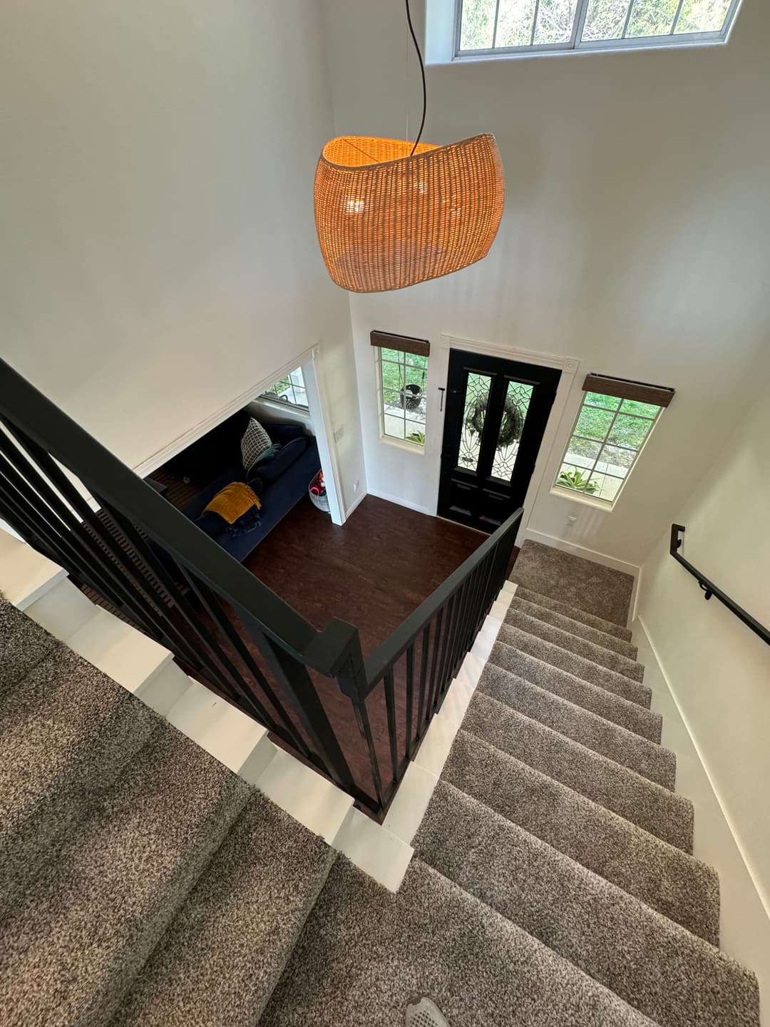 Modern staircase with carpet, stylish pendant light, and view of entryway and living room.