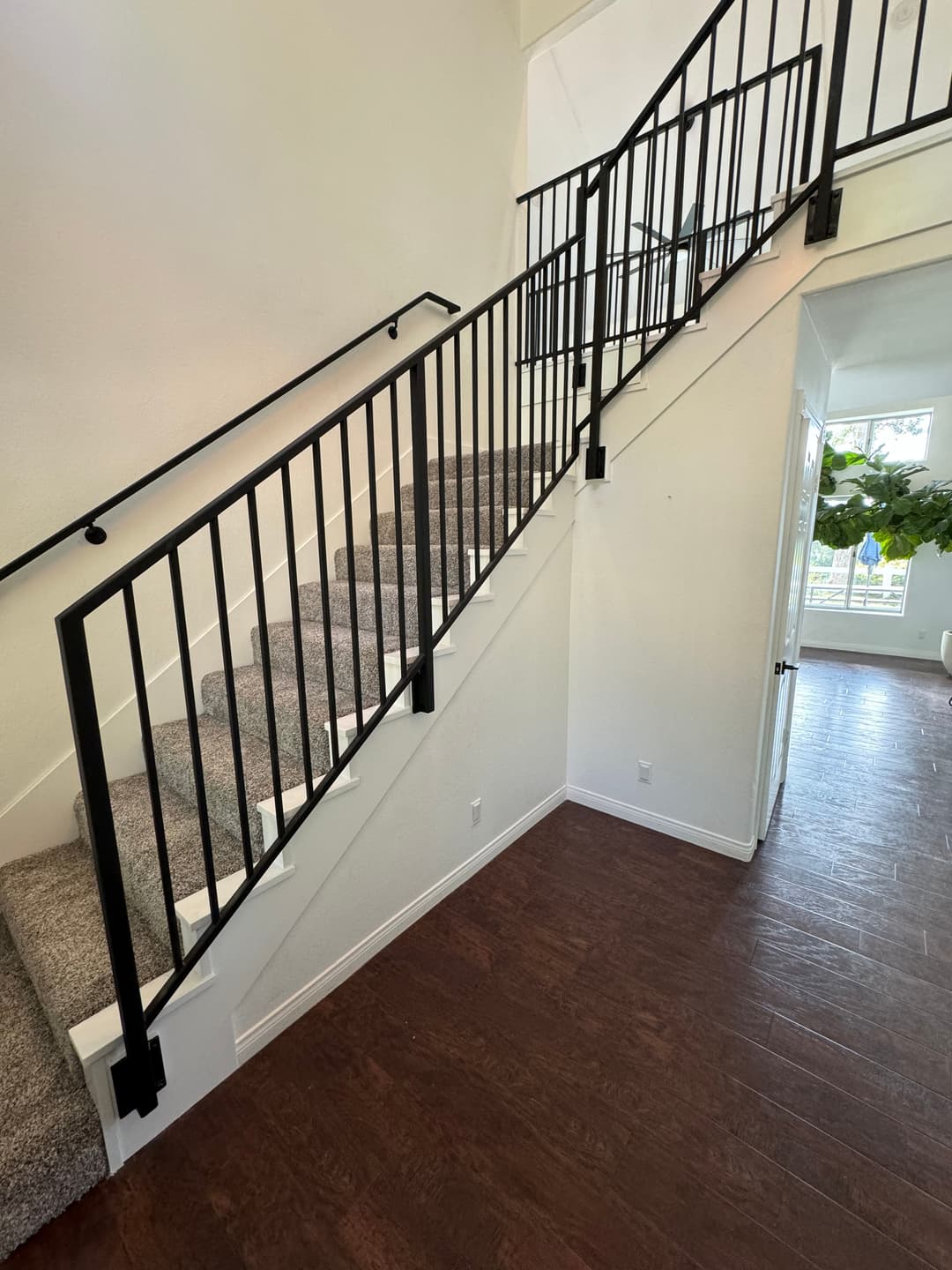 Modern staircase with black metal railing and carpeted steps, bright hallway in background.