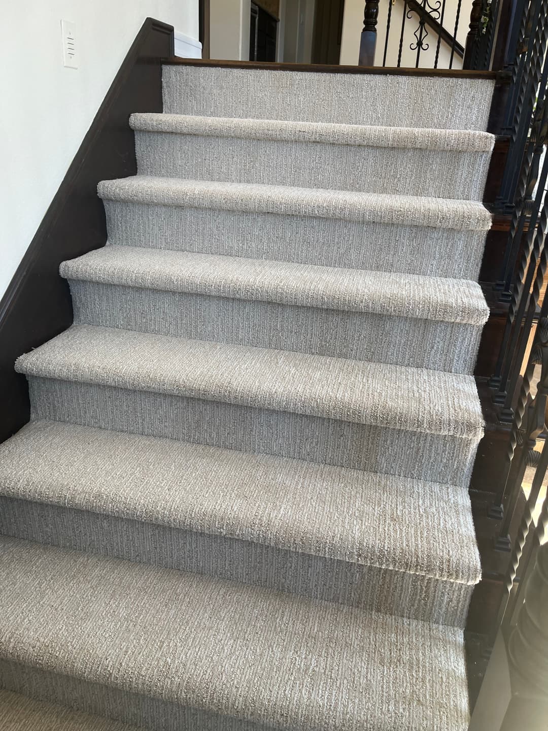 Carpeted staircase with a neutral tone, featuring a wooden railing and natural light.