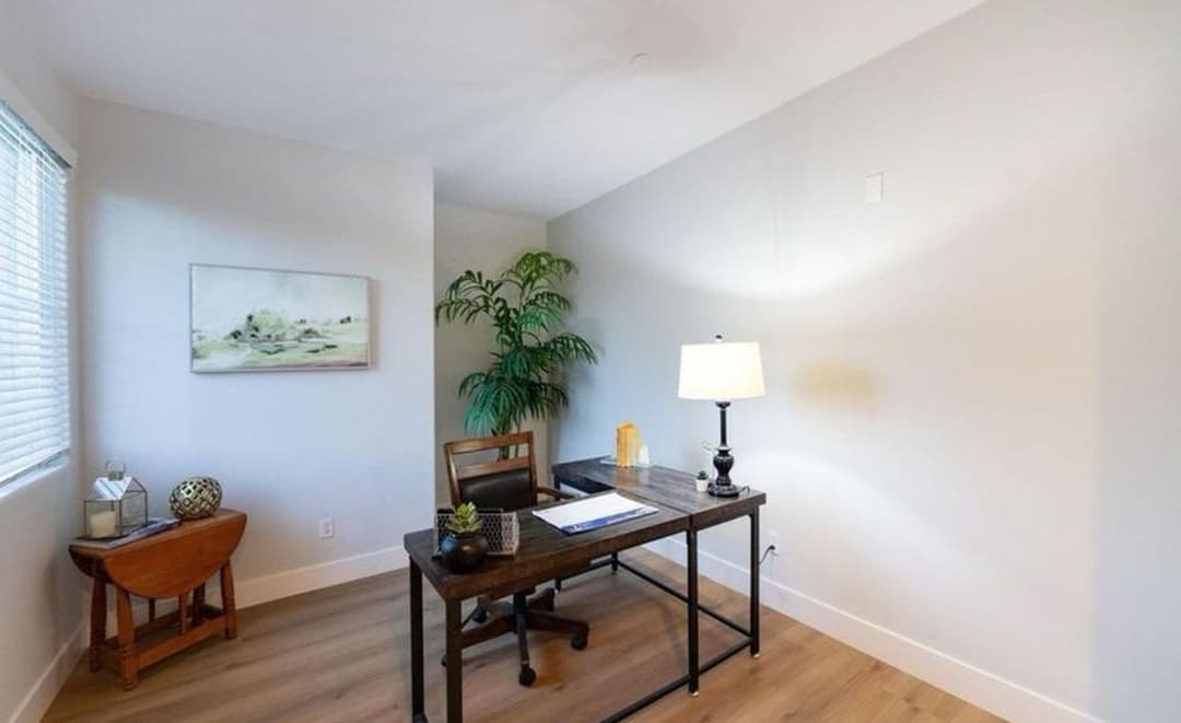 Modern home office with a wooden desk, lamp, potted plant, and minimalist decor.