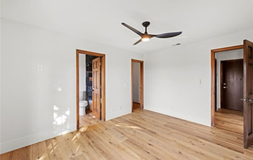 Spacious modern bedroom with wooden floors, ceiling fan, and white walls.