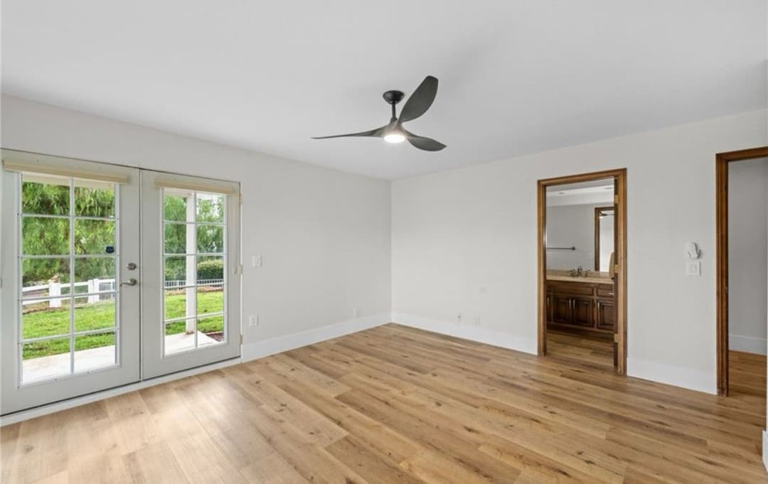 Bright, spacious living room with wooden flooring and modern ceiling fan, featuring double doors.