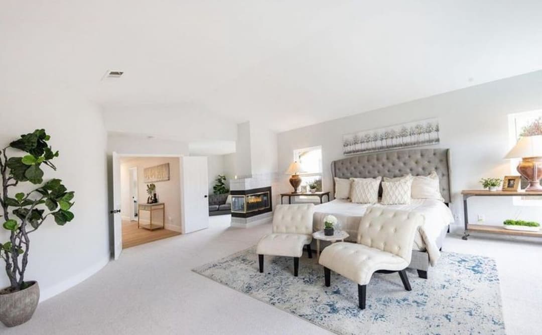 Spacious modern bedroom with stylish bed, armchairs, and decorative plants.