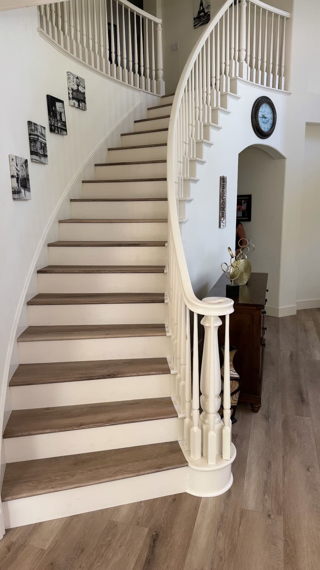 Elegant curved staircase with wooden steps and white railing, leading to a bright entryway.