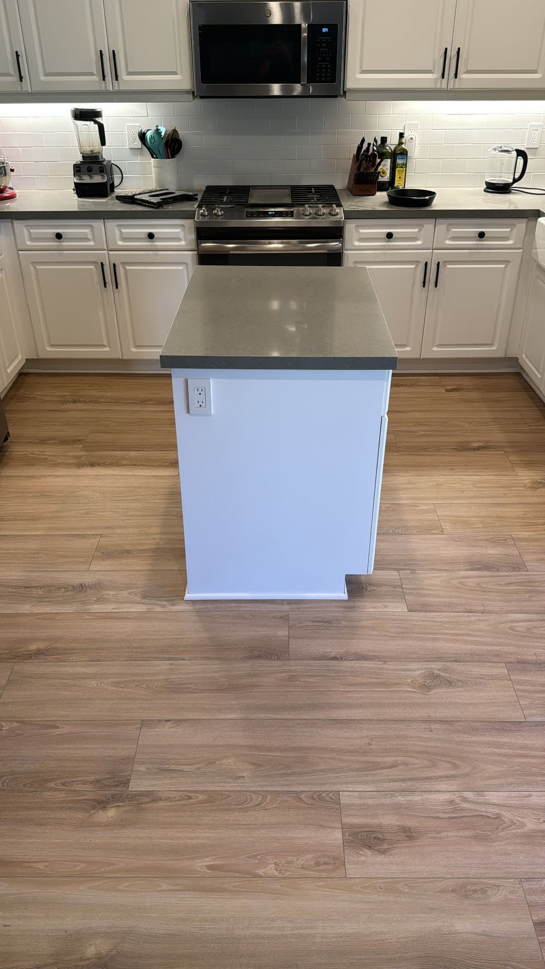 Modern kitchen with white cabinetry, gray countertop island, and wood-look flooring.