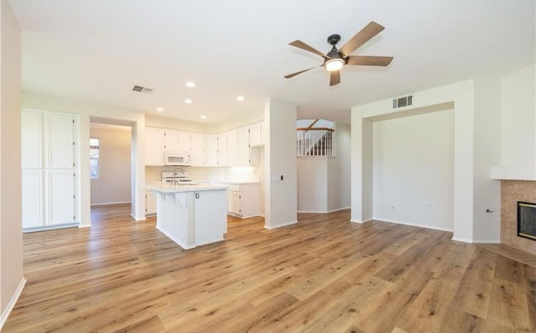 Spacious modern living room with kitchen, hardwood floors, ceiling fan, and natural light.