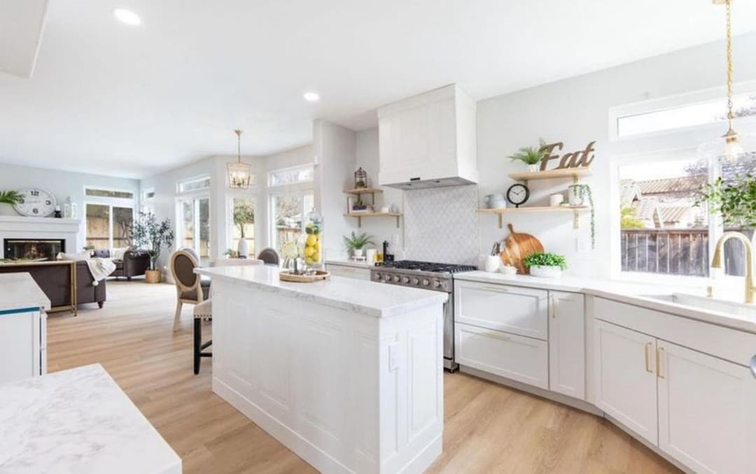 Modern bright kitchen with white cabinetry, marble island, and large windows for natural light.