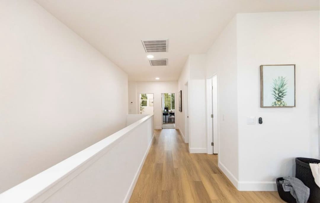 Bright modern hallway with wood flooring and minimalist decor leading to an open room.