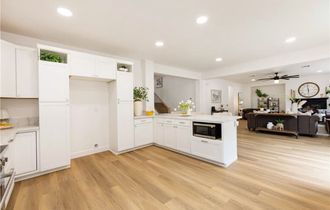 Modern kitchen with white cabinetry, quartz countertops, and open living area with hardwood floors.