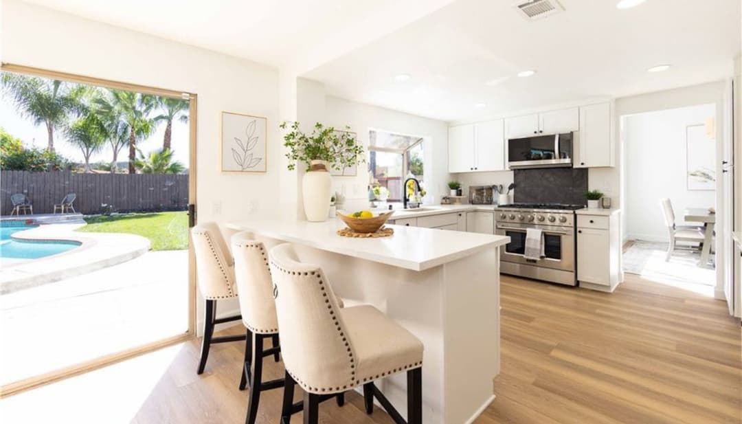 Modern kitchen with white cabinets, bar seating, and pool view in a sunny, open layout.