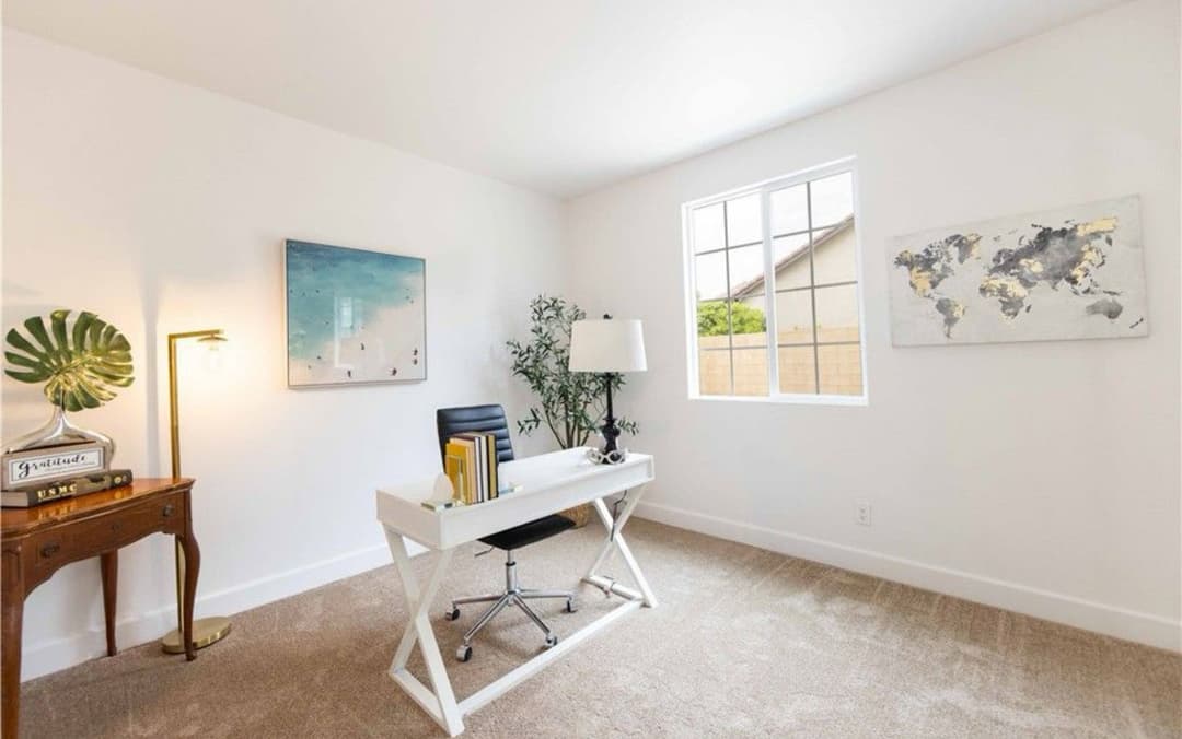 Modern home office with a white desk, chair, art, and large window for natural light.