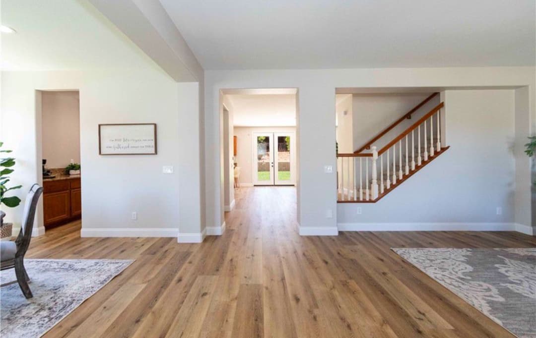 Spacious modern living room with hardwood floors and elegant staircase leading to outdoor view.