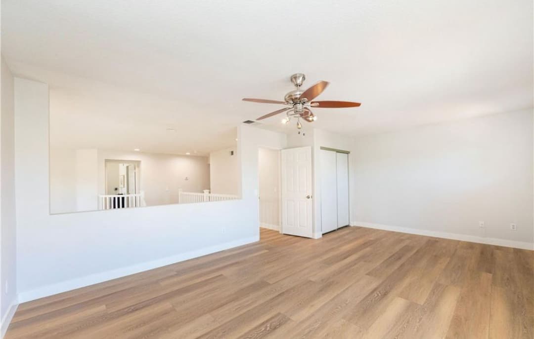 Spacious living room with ceiling fan, hardwood floor, natural light, and neutral tones.