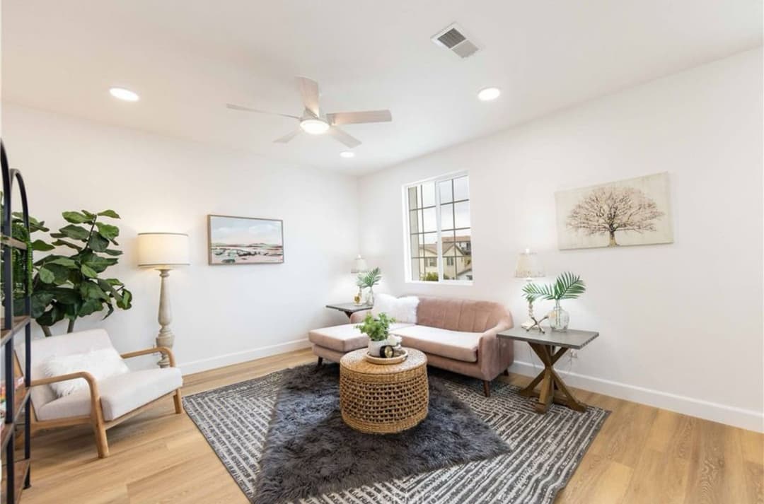 Modern living room with pink sofa, area rug, plants, and natural light from a window.