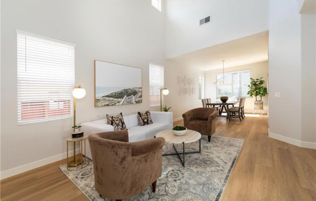 Modern living room with beige sofa, accent chairs, and natural light from large windows.