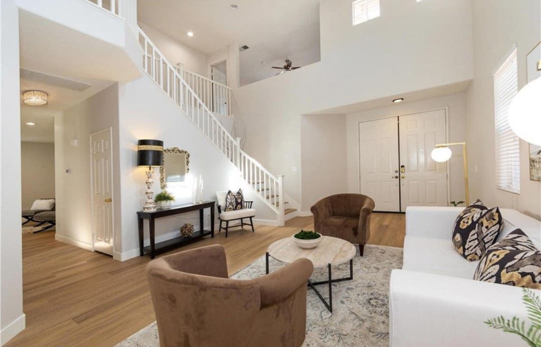 Bright modern living room with a staircase, brown chairs, and a white sofa on wooden flooring.