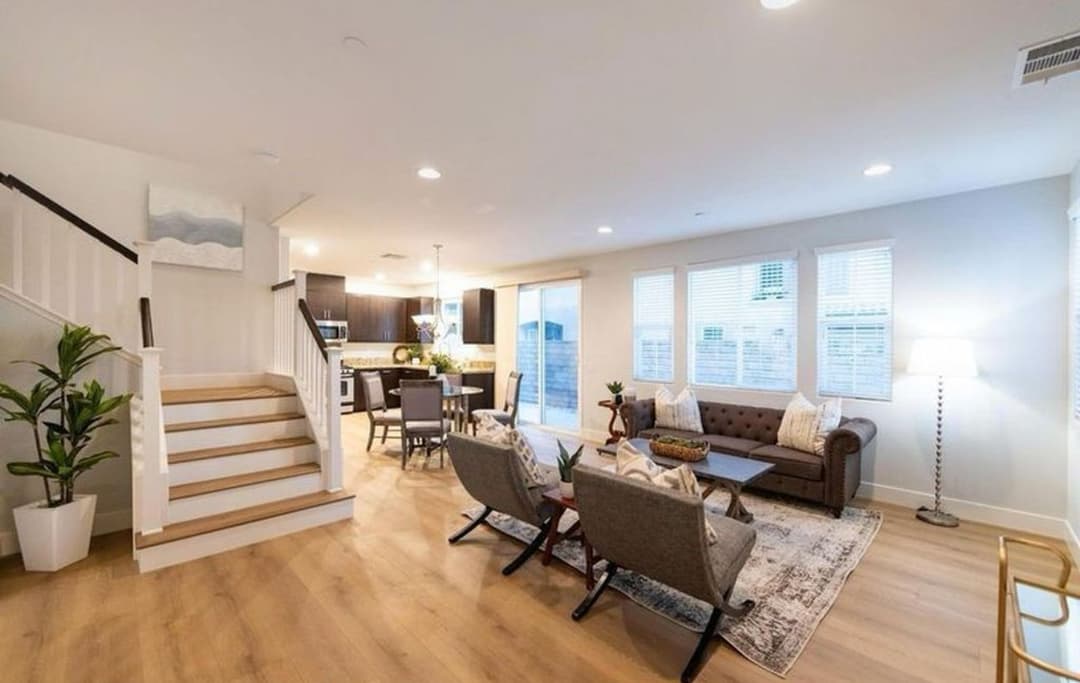 Modern living room with cozy seating, a staircase, and large windows for natural light.