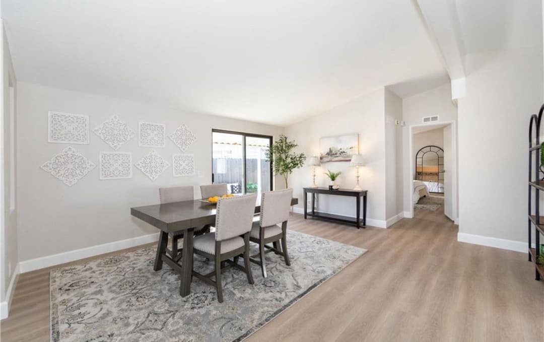 Modern dining room with a large table, light gray walls, and soft natural lighting.