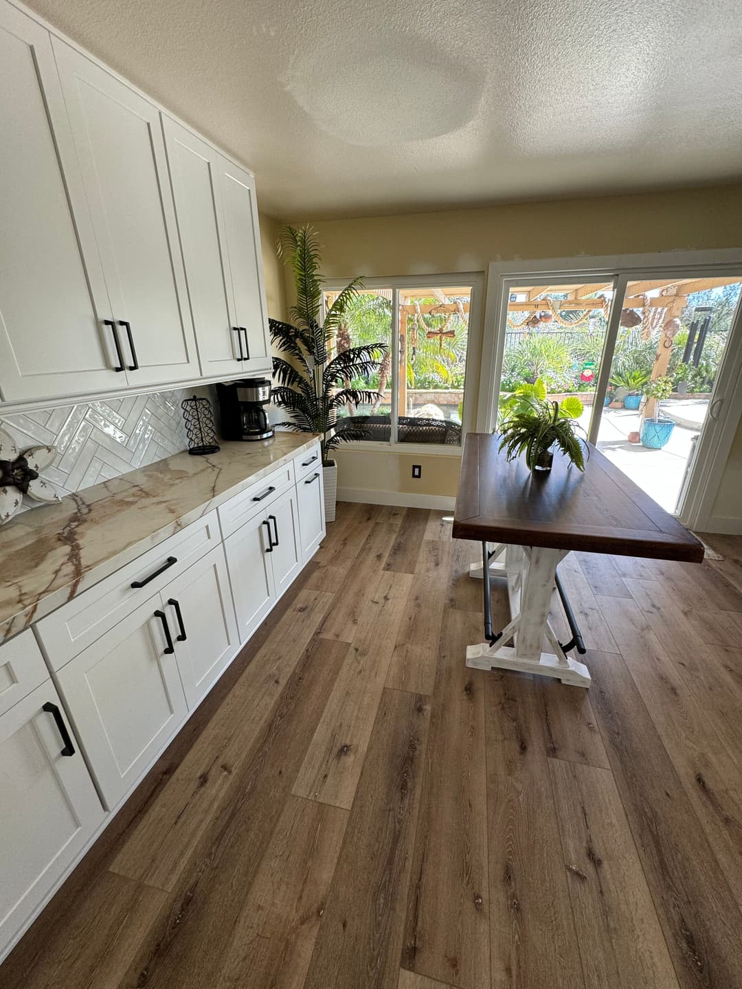 Modern kitchen featuring white cabinets, marble countertops, wooden table, and natural light.