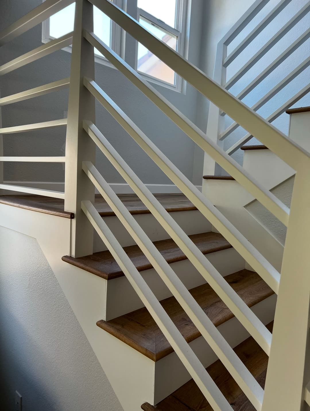 Modern staircase with white railings and wooden steps, illuminated by natural light.