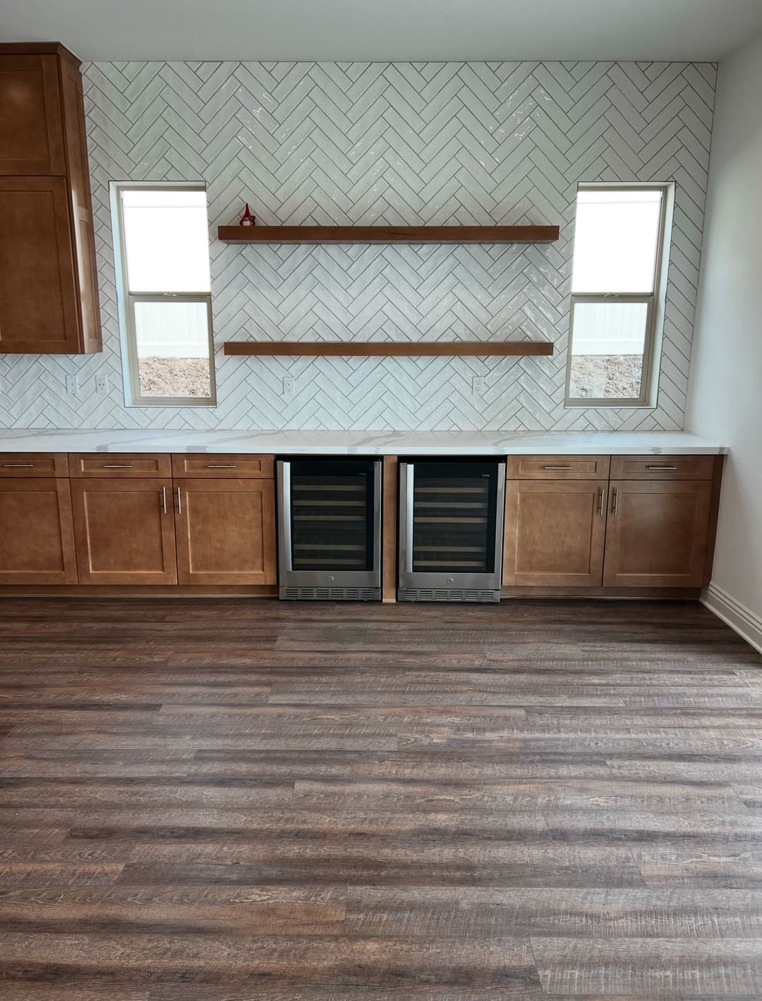 Modern kitchen featuring herringbone tile backsplash, double wine coolers, and wooden cabinets.