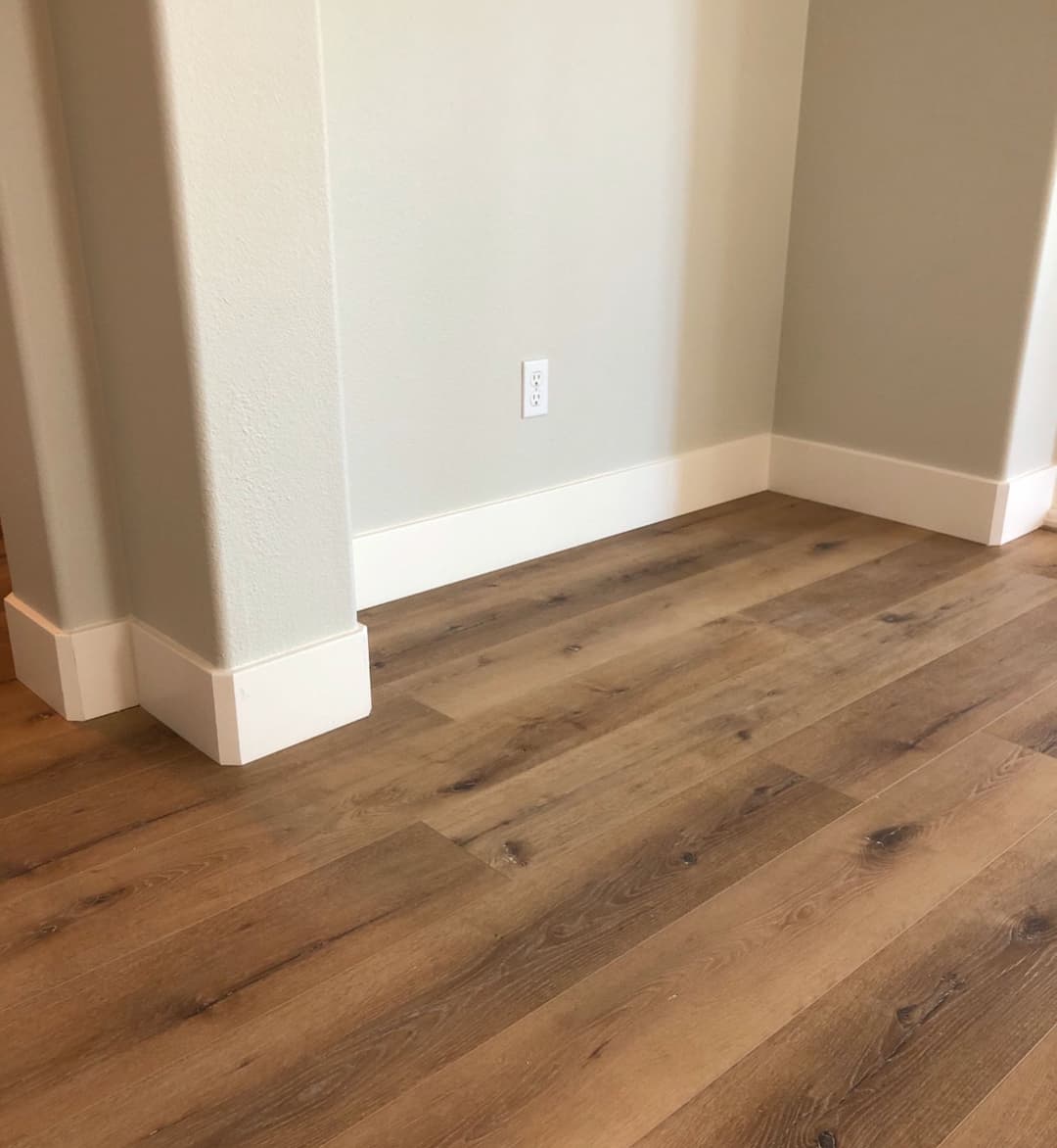 Modern interior corner with elegant trim and stylish laminate flooring. Bright neutral walls.