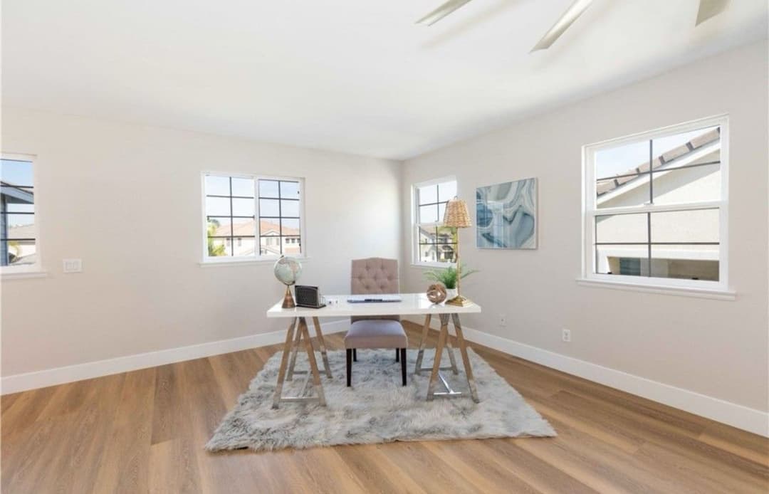 Modern home office with a white desk, stylish chair, and large windows for natural light.