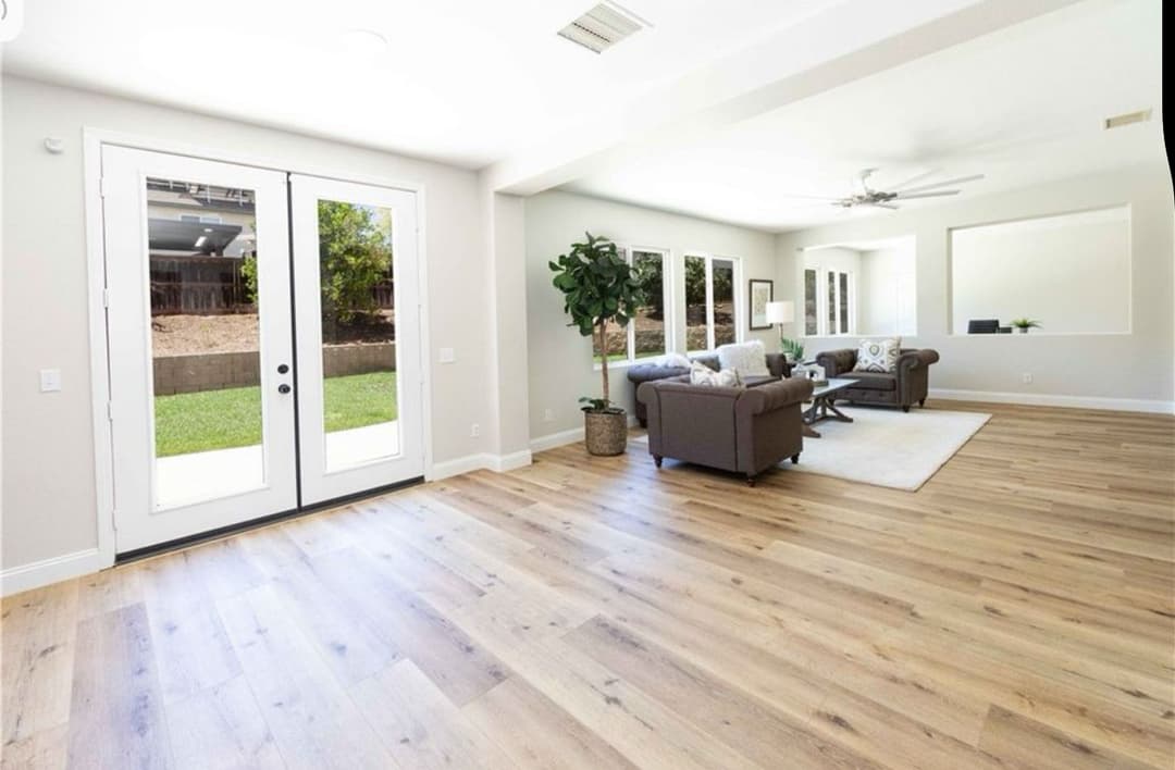 Bright and airy living room with laminate flooring, large windows, and modern furnishings.