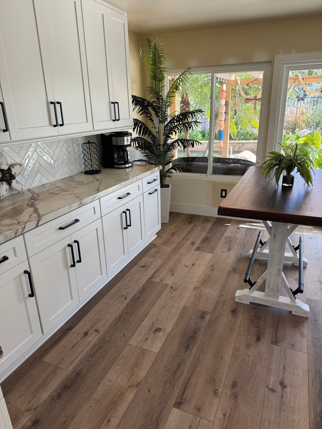 Modern kitchen with white cabinets, marble countertop, and a view of outdoor greenery.