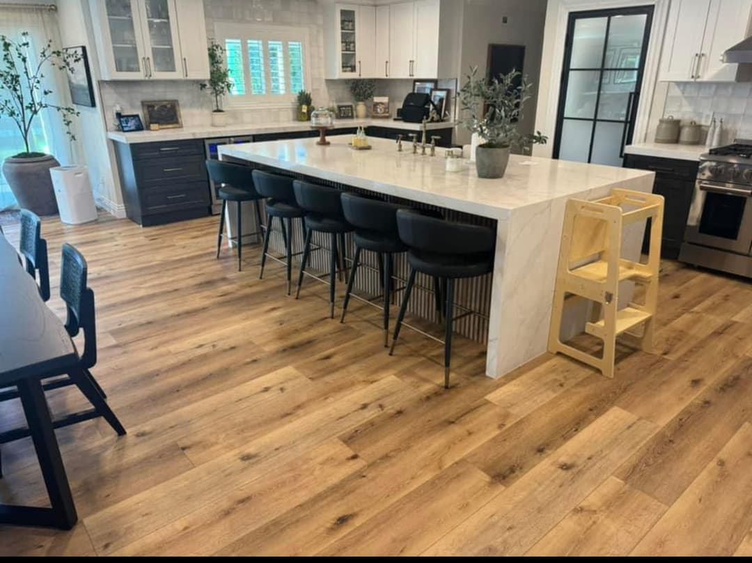 Modern kitchen with large island, black bar stools, light wood flooring, and elegant decor.