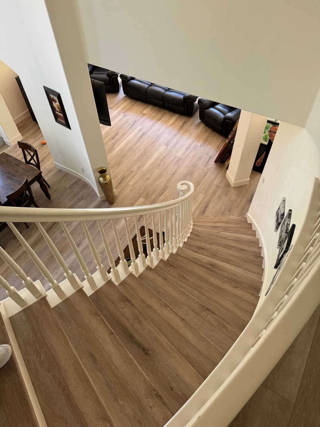 Curved staircase view overlooking a spacious living room with black sofas and wooden floor.