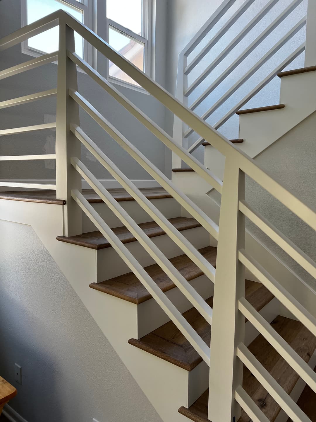 Modern staircase with white railing and wooden steps, bright natural light from windows.