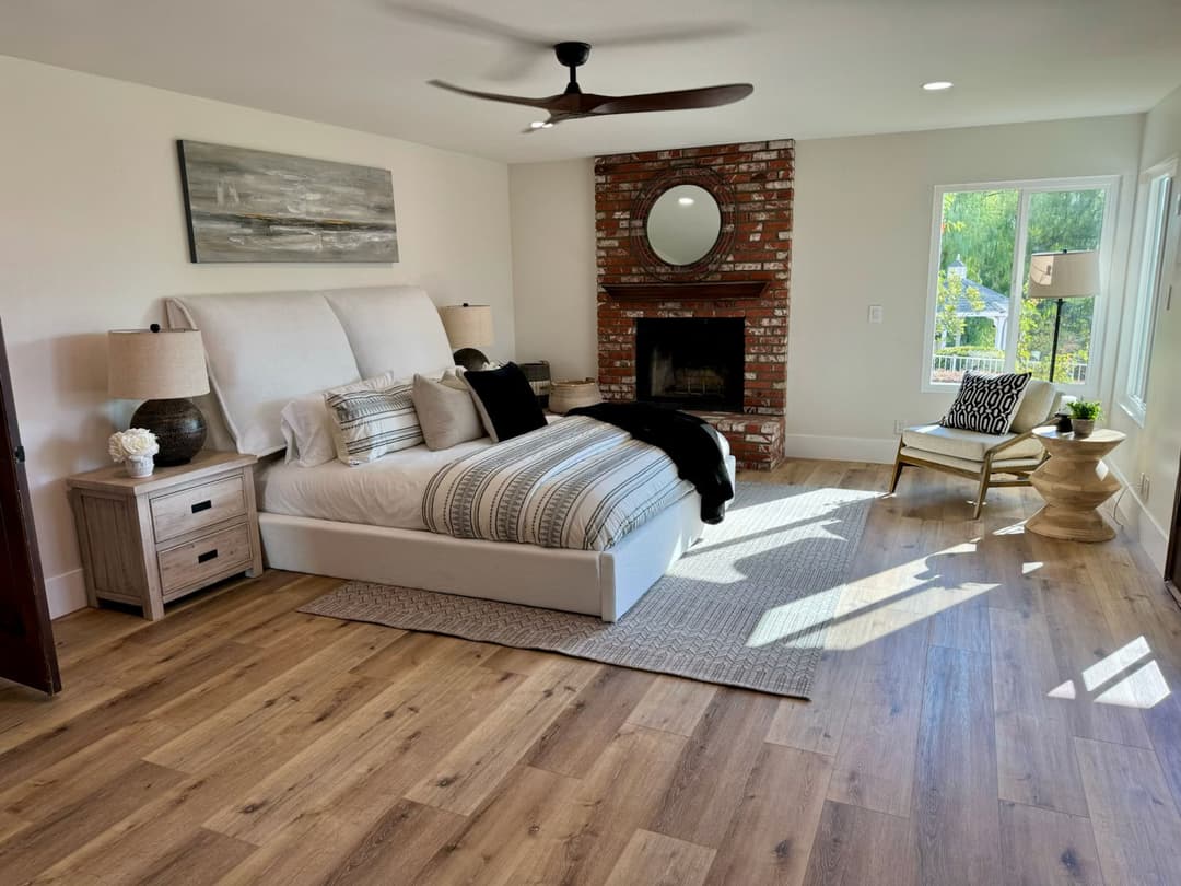 Spacious modern bedroom with a cozy bed, brick fireplace, and natural light from windows.