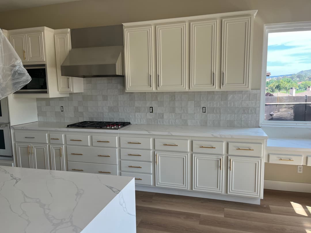 Modern kitchen with white cabinetry, marble countertop, and stainless steel appliances.