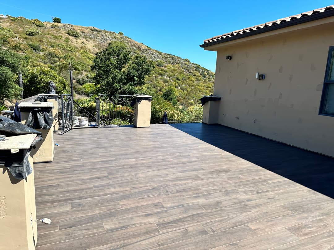 Newly renovated outdoor deck with wood-like flooring overlooking a green hillside.