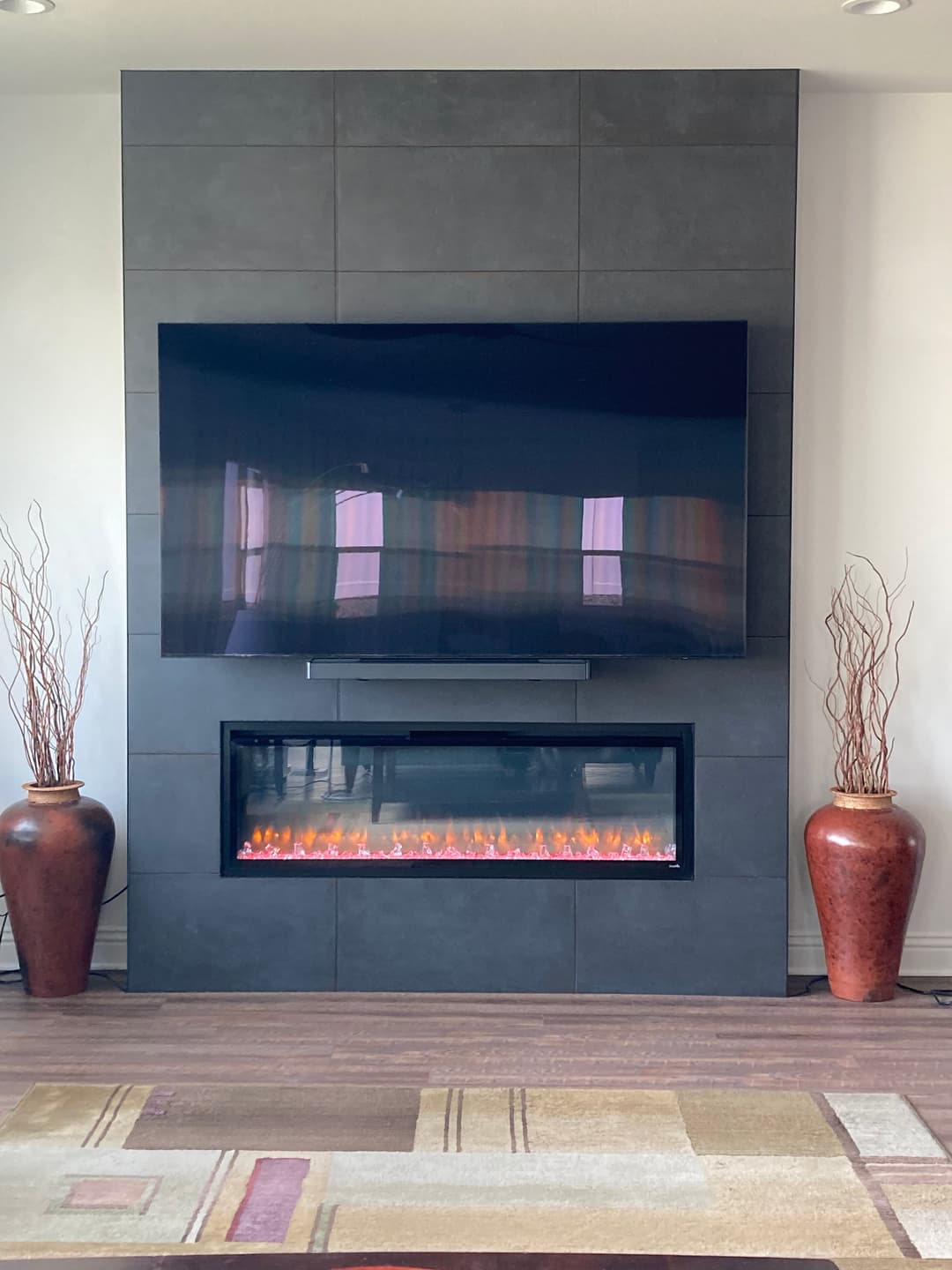 Modern living room with a sleek wall-mounted TV above an electric fireplace and decorative vases.