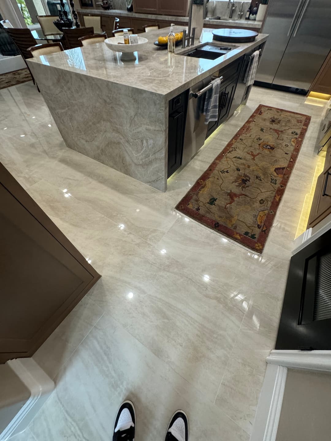 Modern kitchen with marble floor, dark cabinetry, and a patterned area rug. Bright and spacious.