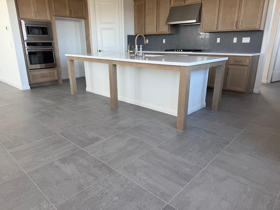 Modern kitchen interior featuring a large island with light wood finish and gray tile flooring.