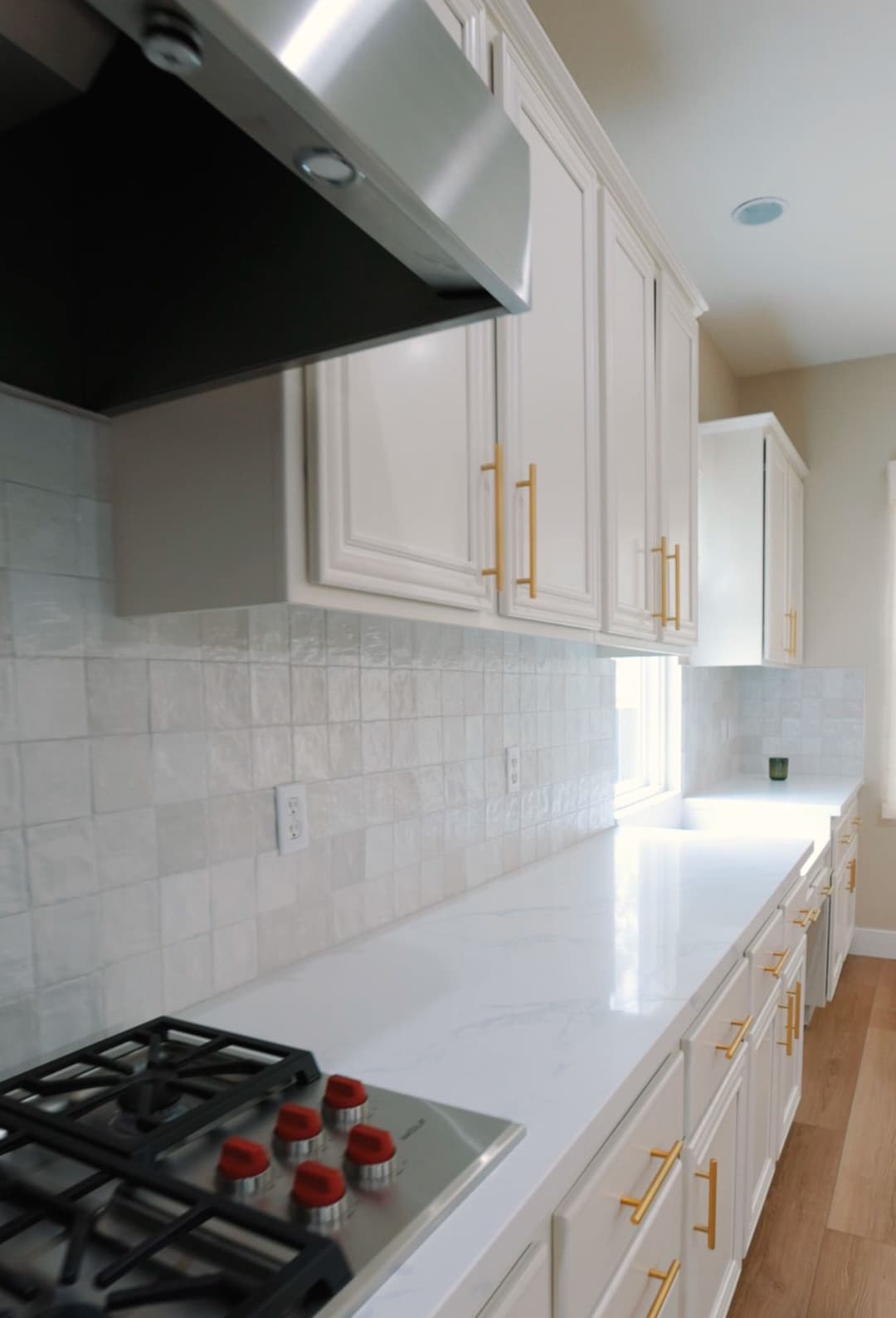 Modern kitchen with white cabinets, gold handles, and marble countertop. Gas stove in view.
