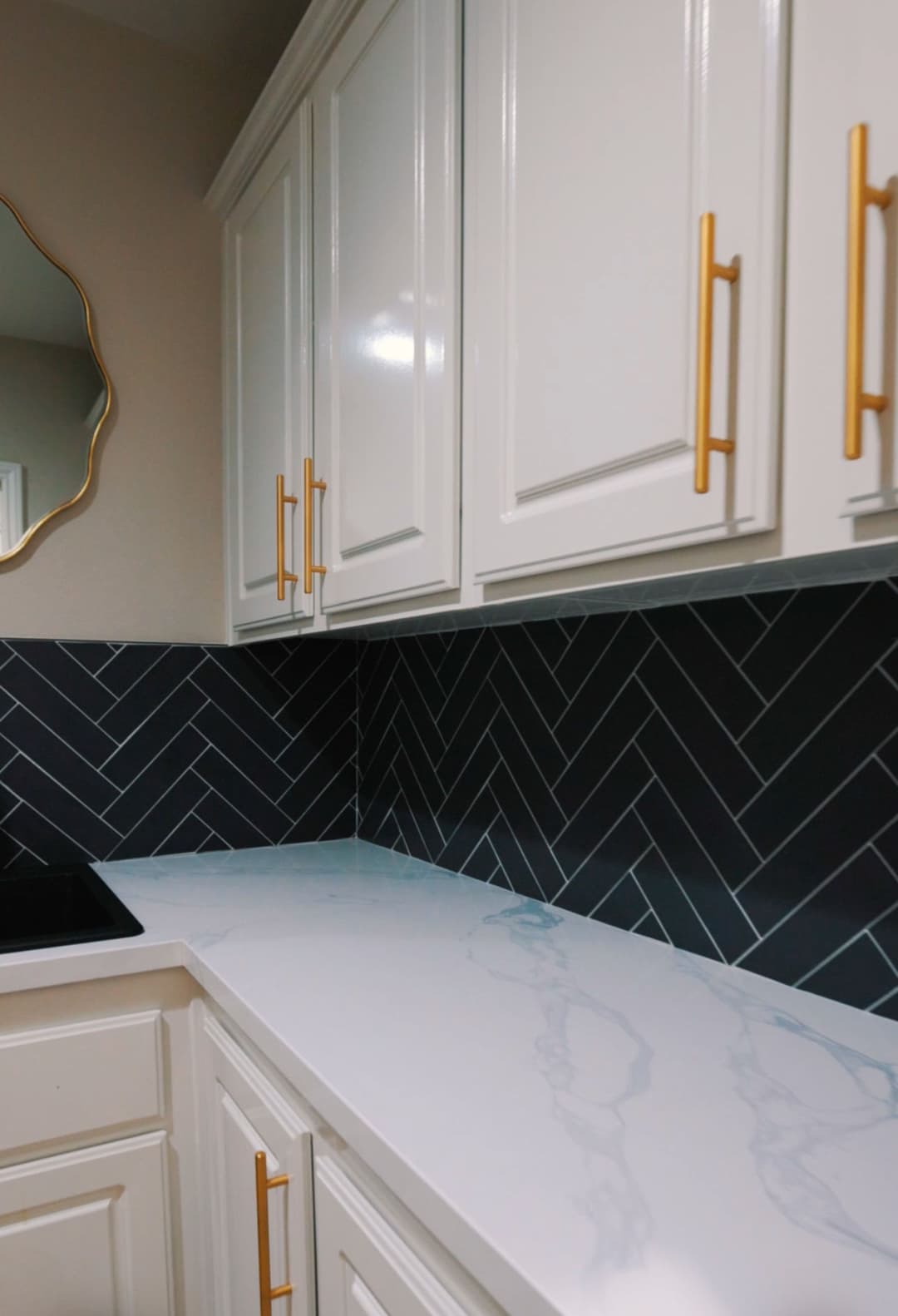 Stylish kitchen with white cabinets, herringbone backsplash, and gold handles for modern design.