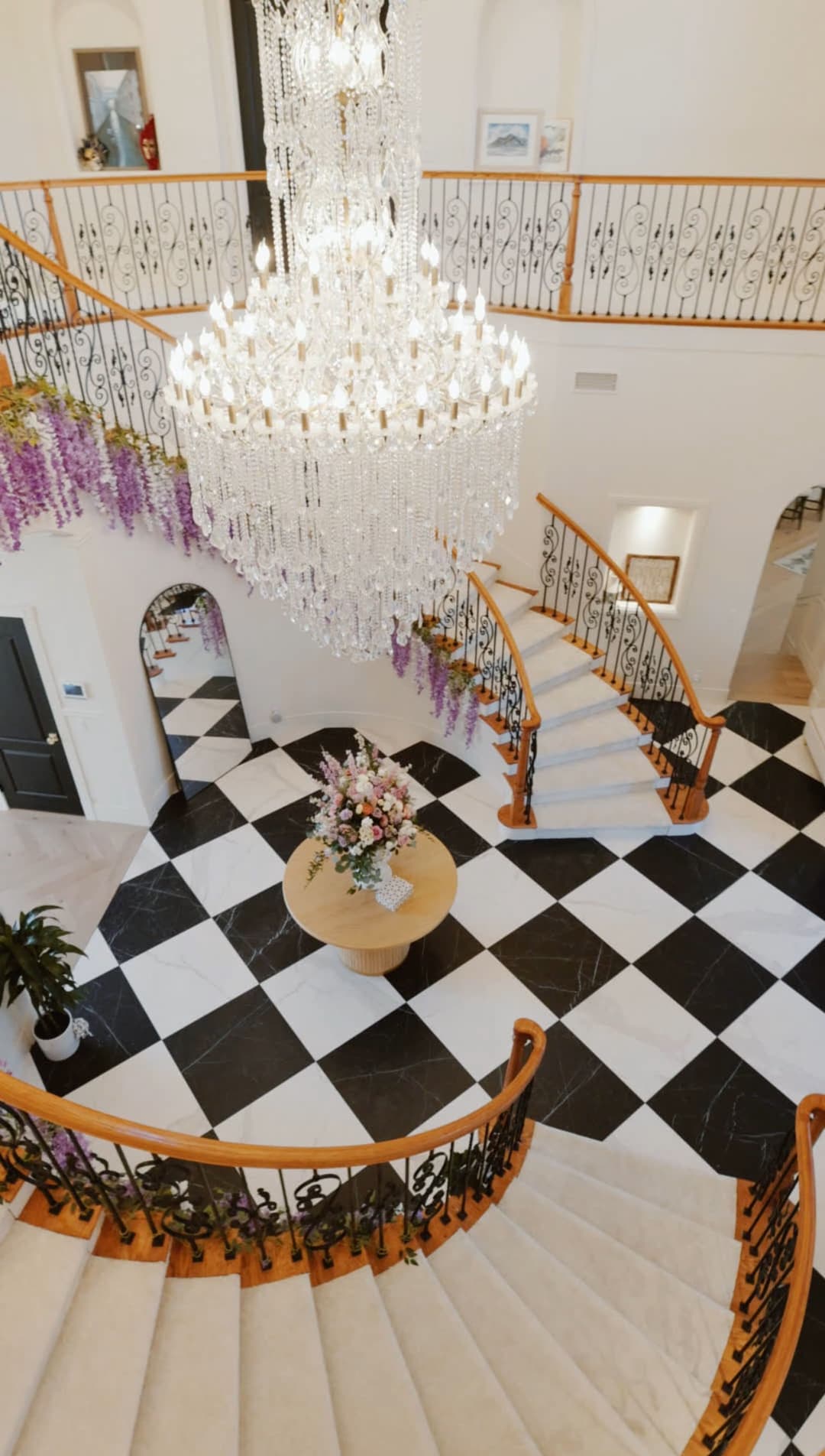 Elegant foyer with chandelier, floral arrangements, and spiral staircase in a luxurious home.