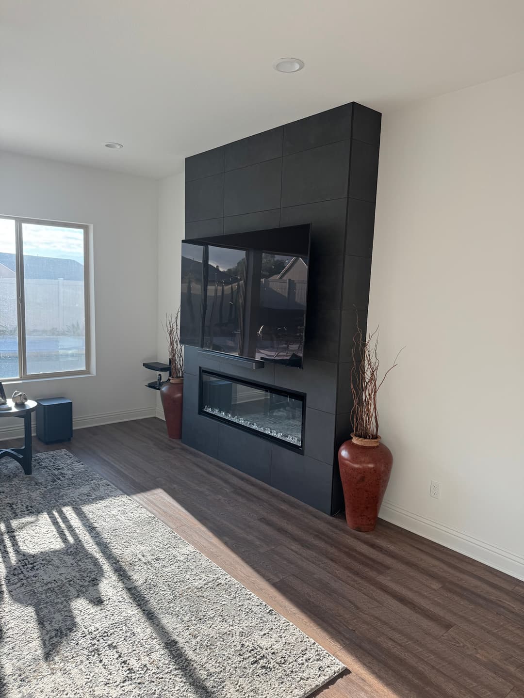 Modern living room featuring a black tiled accent wall with a TV and a glass-fronted fireplace.