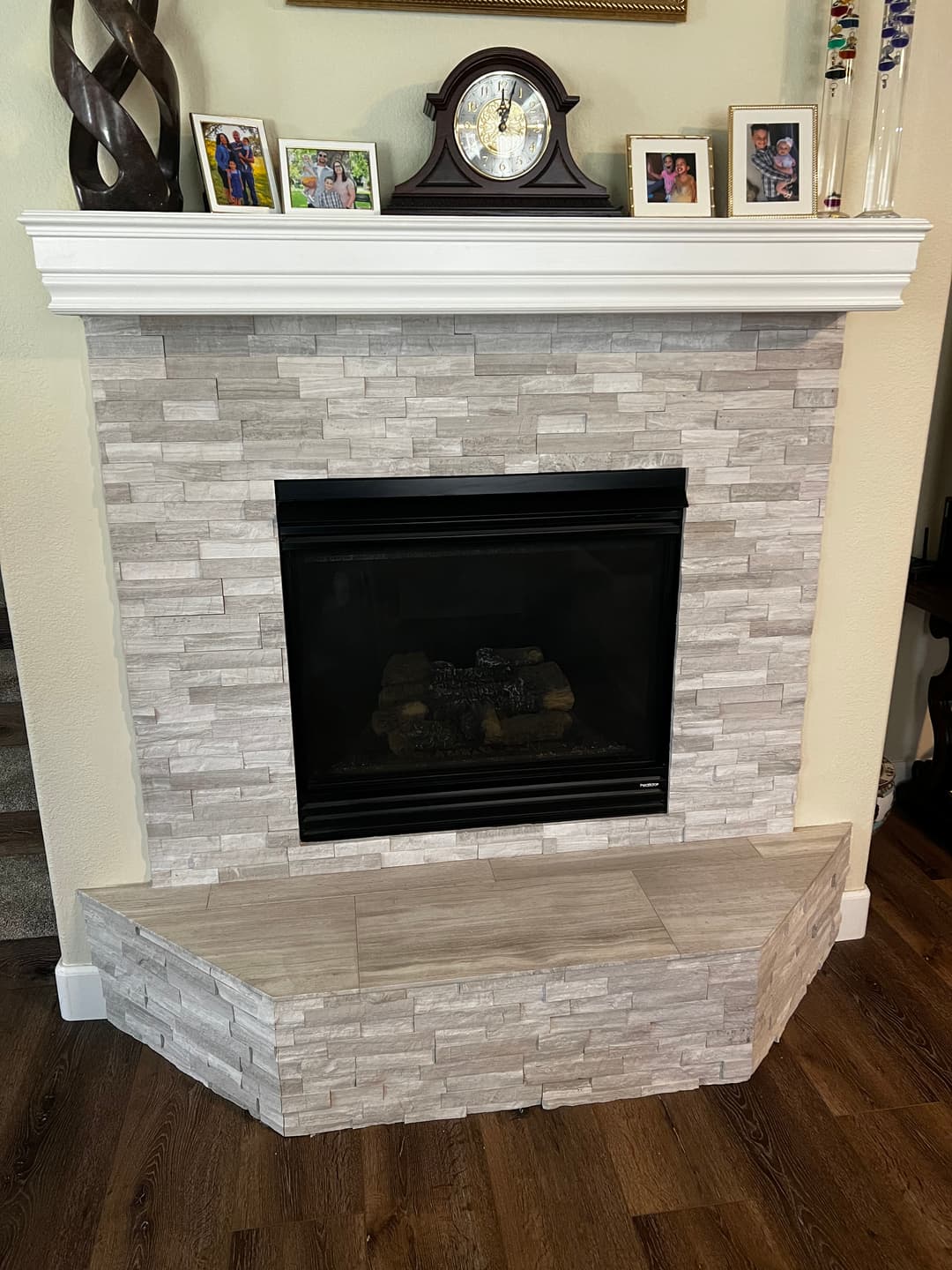 Modern stone fireplace with a white mantel, clock, and family photos on the wall.
