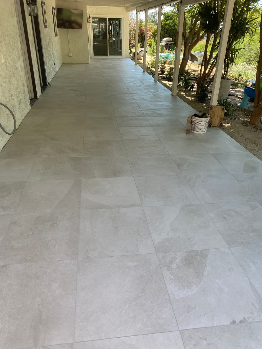 Newly installed light gray tile flooring on a covered patio with garden view.