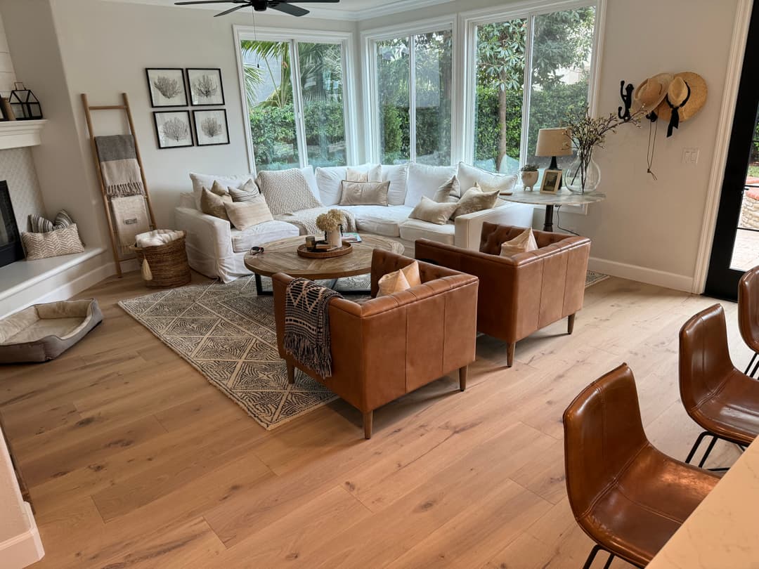 Modern living room with white sectional sofa, brown leather chairs, and large windows.
