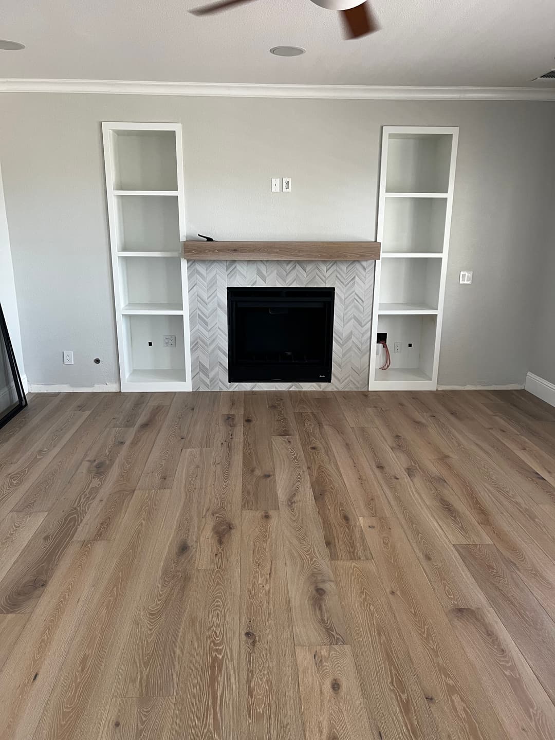 Living room with light wood flooring, modern fireplace, and built-in shelves against gray walls.