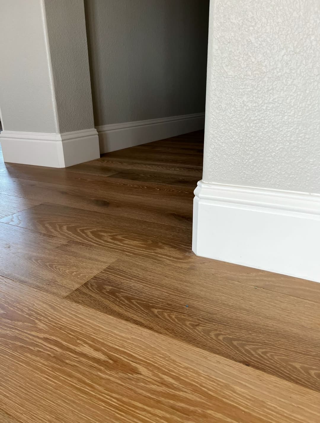 Close-up of new hardwood flooring with white baseboards in a modern interior.
