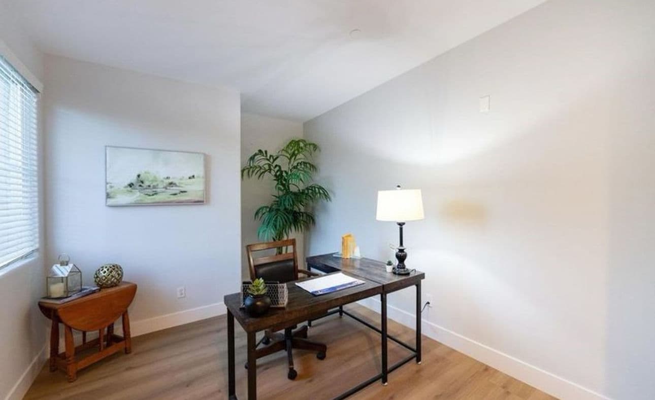 Modern office space featuring a desk, lamp, plant, and artwork on the wall. Bright and minimalist.