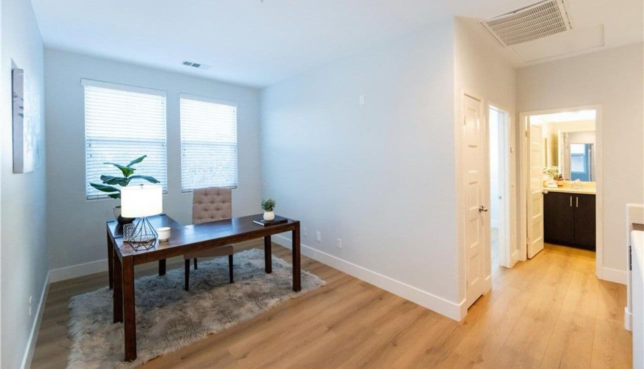 Modern home office with a wooden desk, chair, potted plant, and light-colored walls.